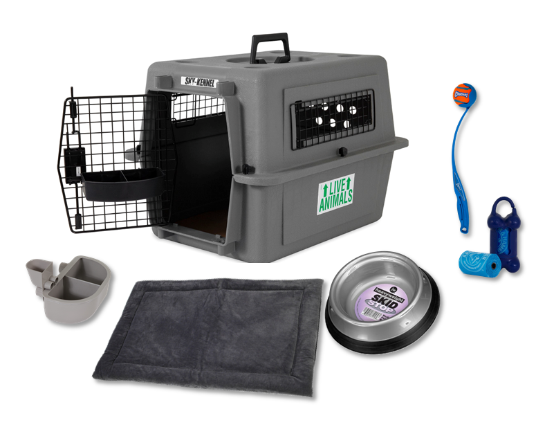 The Pet-mates Essential New Dog Bundle by Pet-mates, shown on a white background, includes a gray pet carrier with an open metal door, food and water bowls, kennel mat, metal dish, blue chew toy, and a dog ball launcher with orange ball.