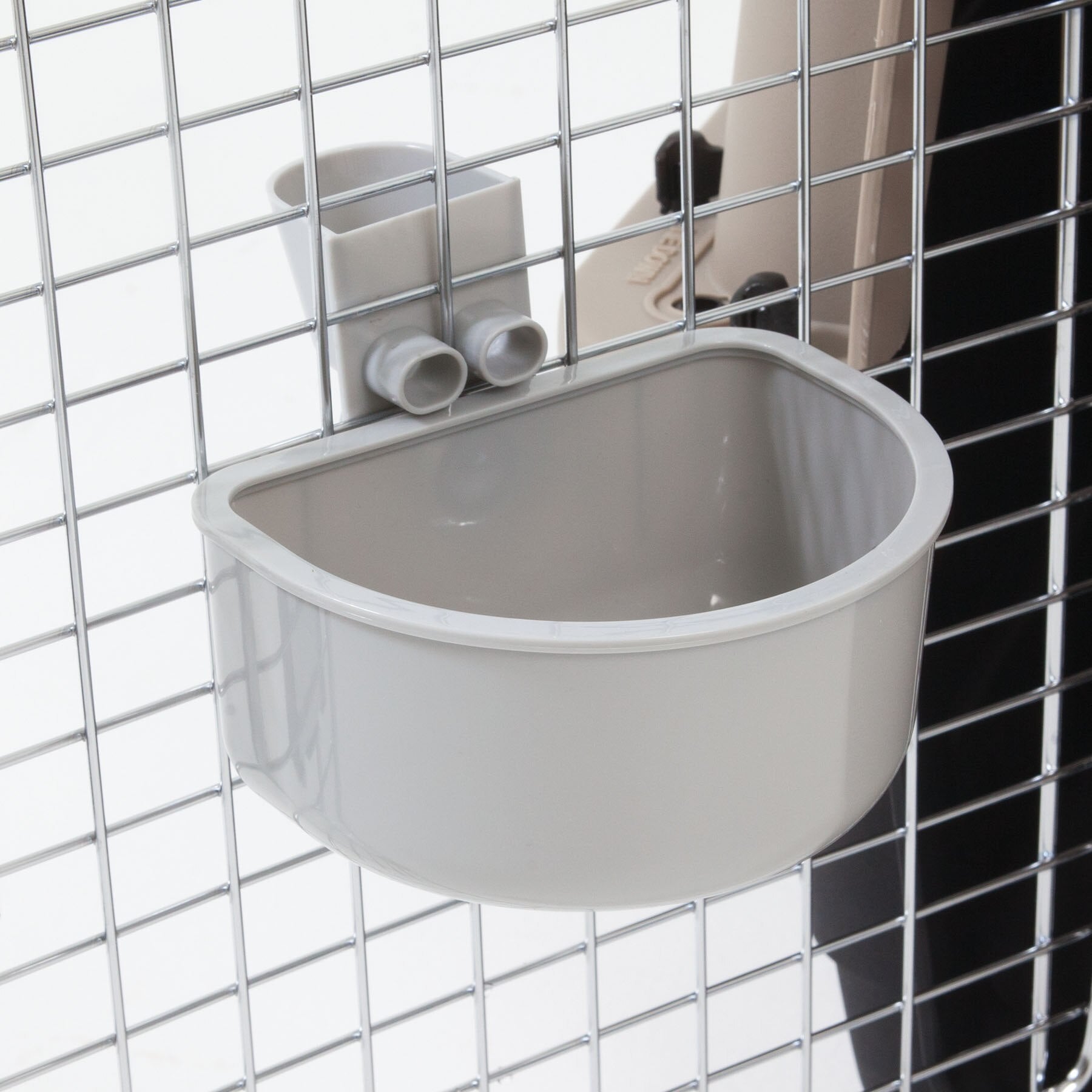 The Pet-mates No Spill Kennel Cup, in beige, mounts securely to a metal wire cage with square openings using a sturdy bracket. This rounded rectangular bowl from Pet-mates is perfect for pets and provides convenience as an efficient travel water bowl.