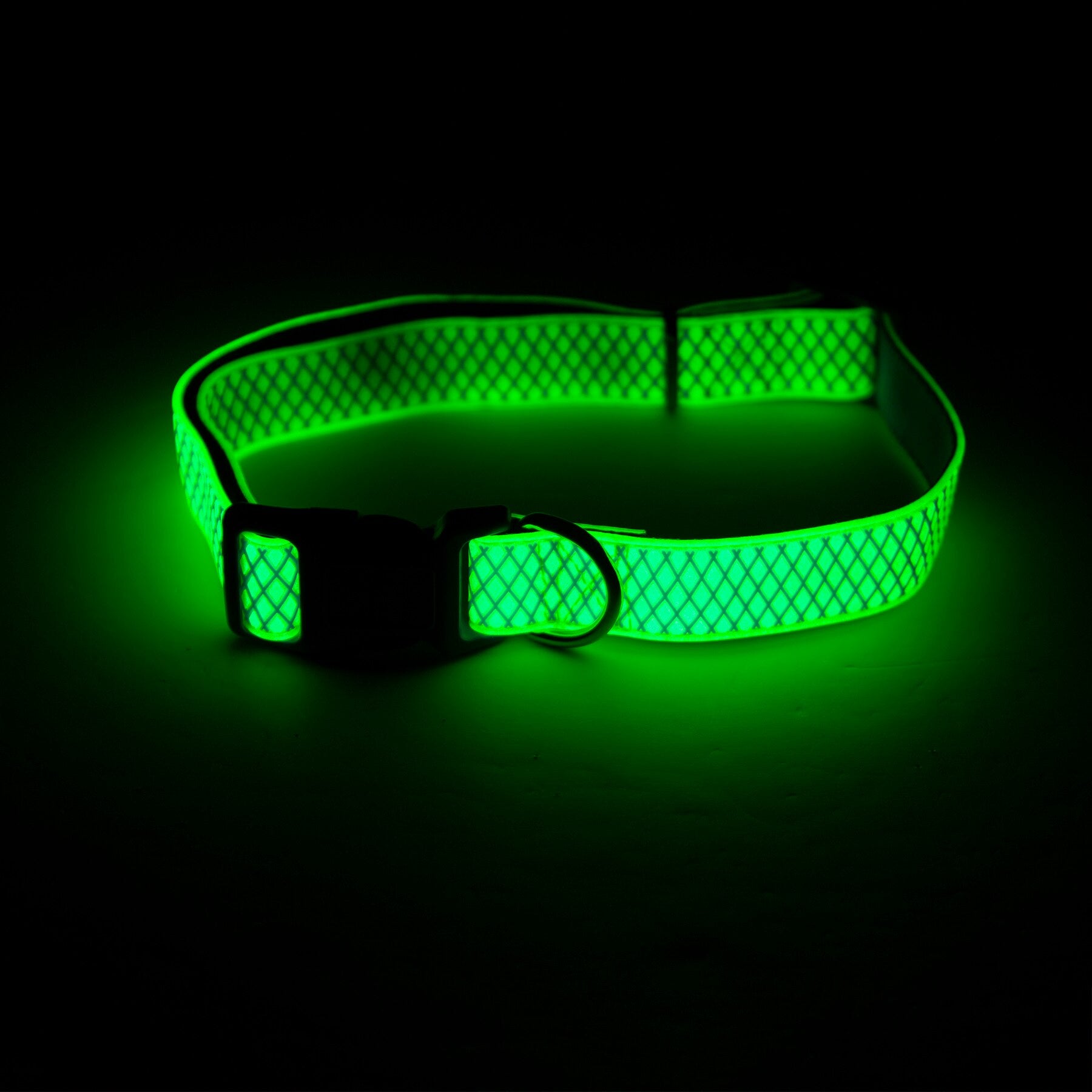 The Pet-mates Green Grid Glow in the Dark Dog Collar features a grid pattern and emits a bright glow, highlighting its texture, metallic buckle, and D-ring against a dark surface.