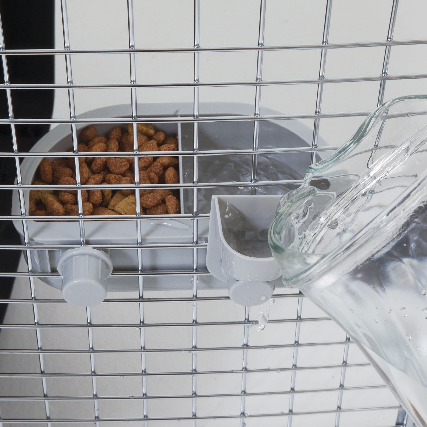 The Pet-mates No Spill Kennel Cup Double Diner provides hydration and nourishment to pets in metal cages, featuring a water pitcher for easy filling and a feeding tray for brown pet food. This setup ensures pets stay nourished and hydrated on the go with BPA and lead-free materials.
