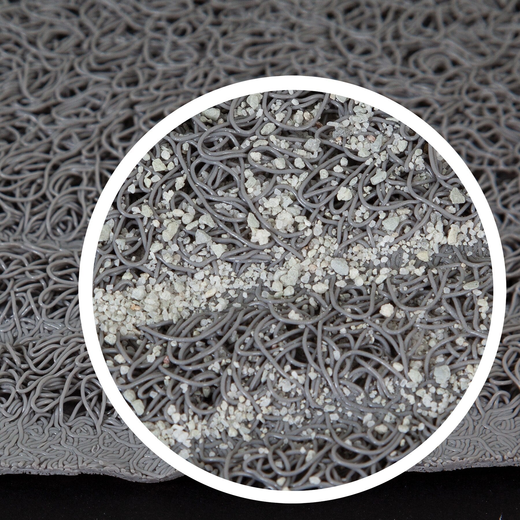 The close-up of the Pet-mates Litter Mat Circles Design by Pet-mates shows a textured gray surface with tangled loops resembling spaghetti, featuring a subtle webbed design. A circular area highlights small particles scattered over the loops, creating a speckled look against the solid black background.