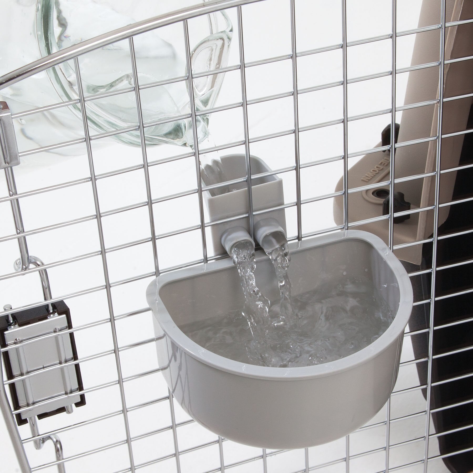The Pet-mates No Spill Kennel Cup by Pet-mates is a gray automatic water dispenser attached to a metal cage, featuring a transparent bottle and dual spouts for spill-proof travel convenience.